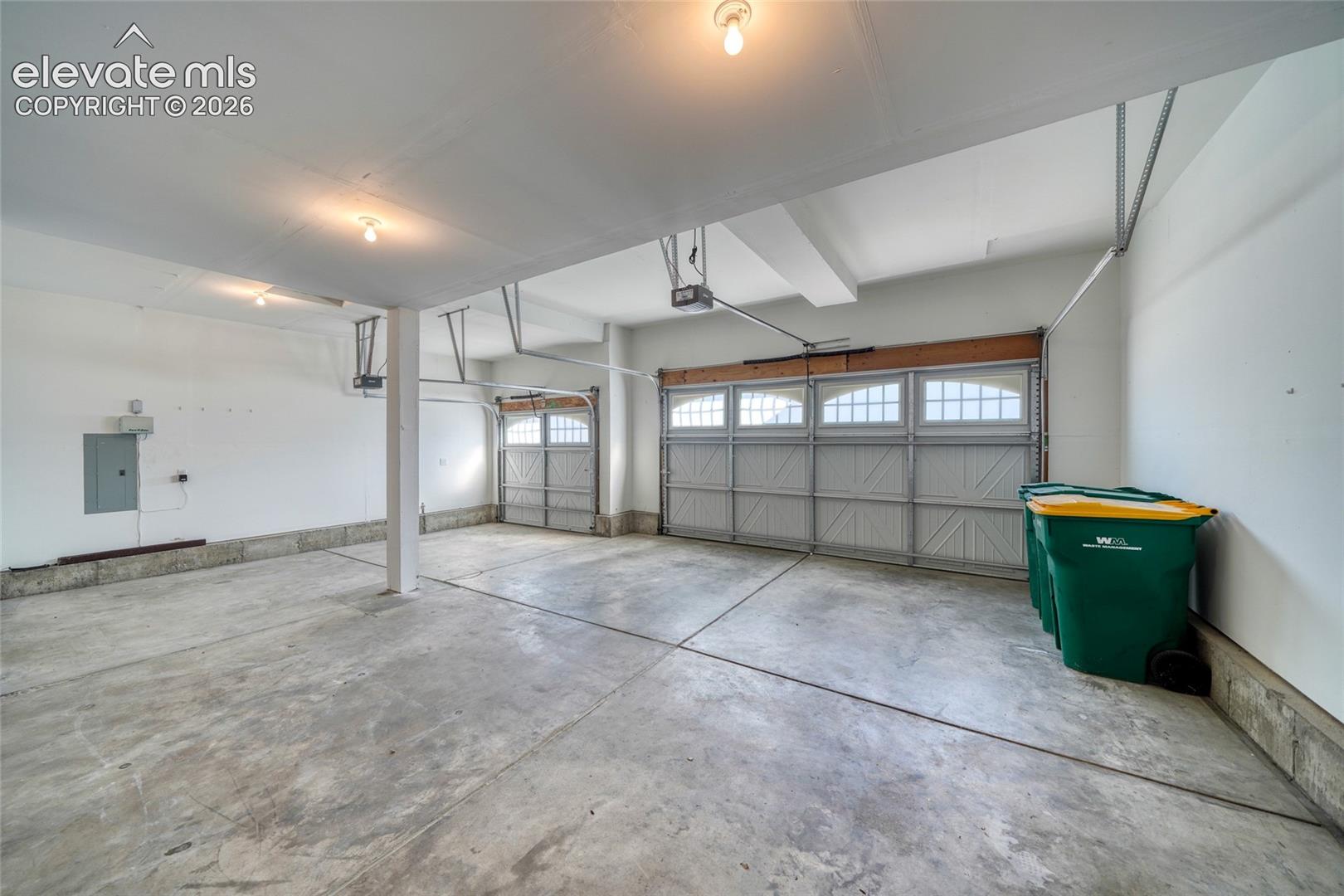 Spacious garage with concrete flooring, two overhead doors featuring upper window panels, and a painted finished ceiling