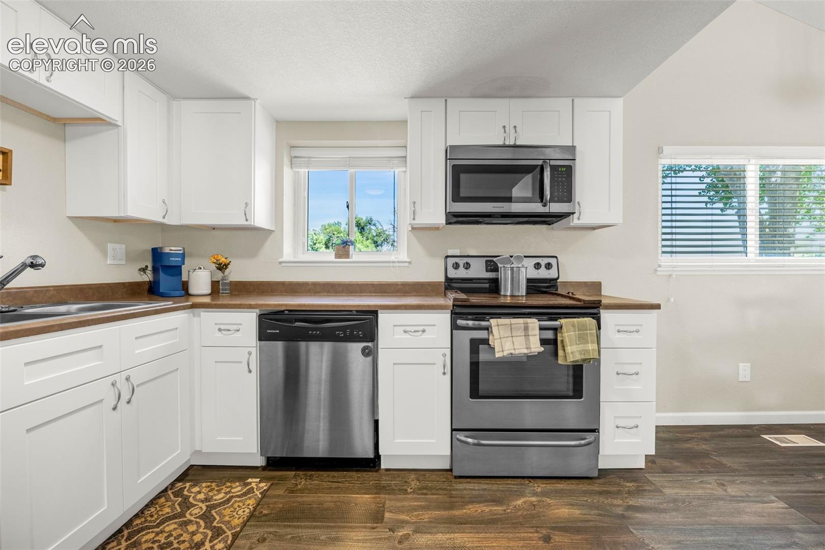 Kitchen featuring white shaker-style cabinetry, stainless steel appliances, wood-finish flooring, and solid-surface countertops