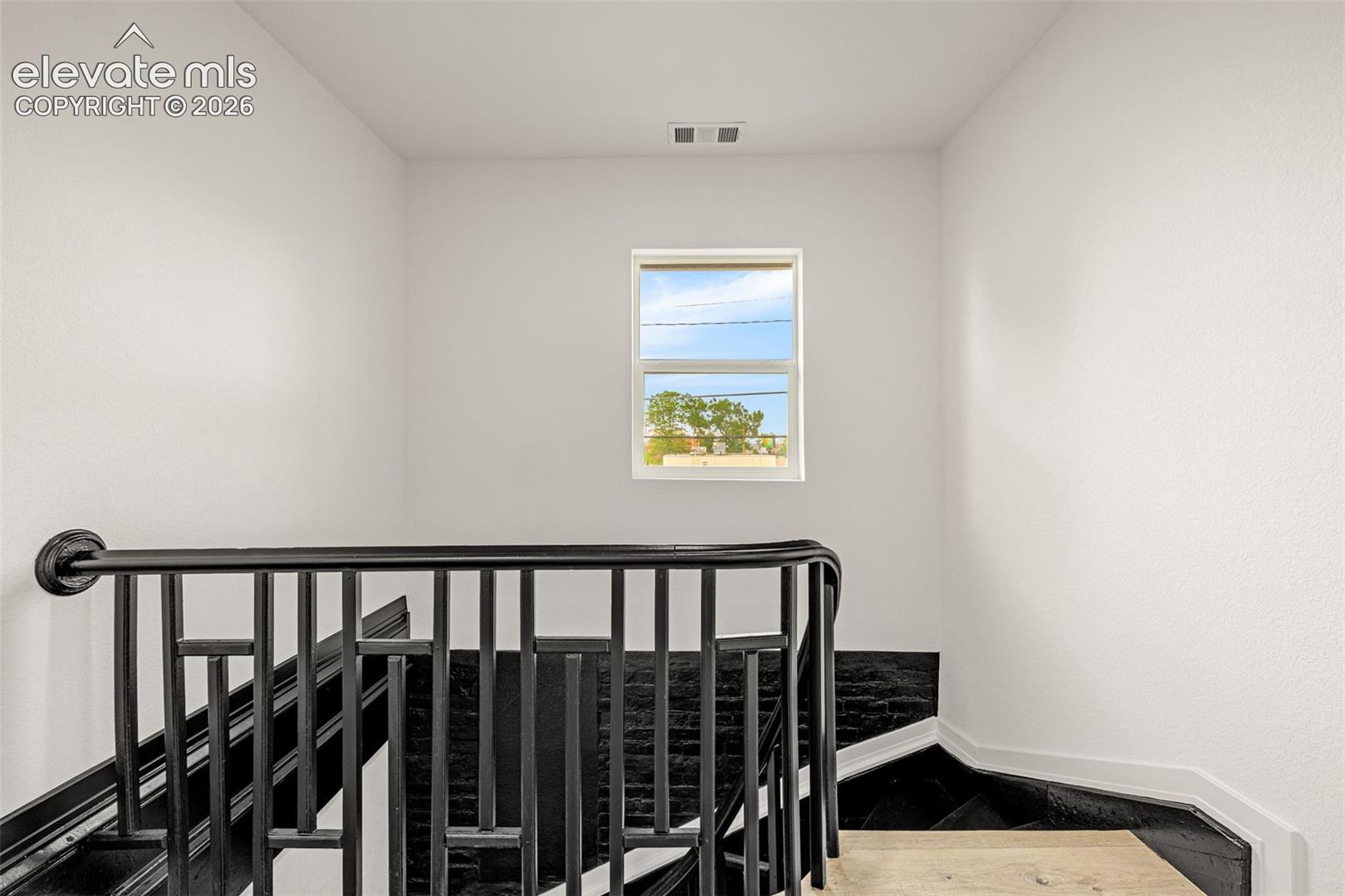 Staircase featuring dark wood-finish treads, a black metal railing, and light wood-finish flooring on the landing