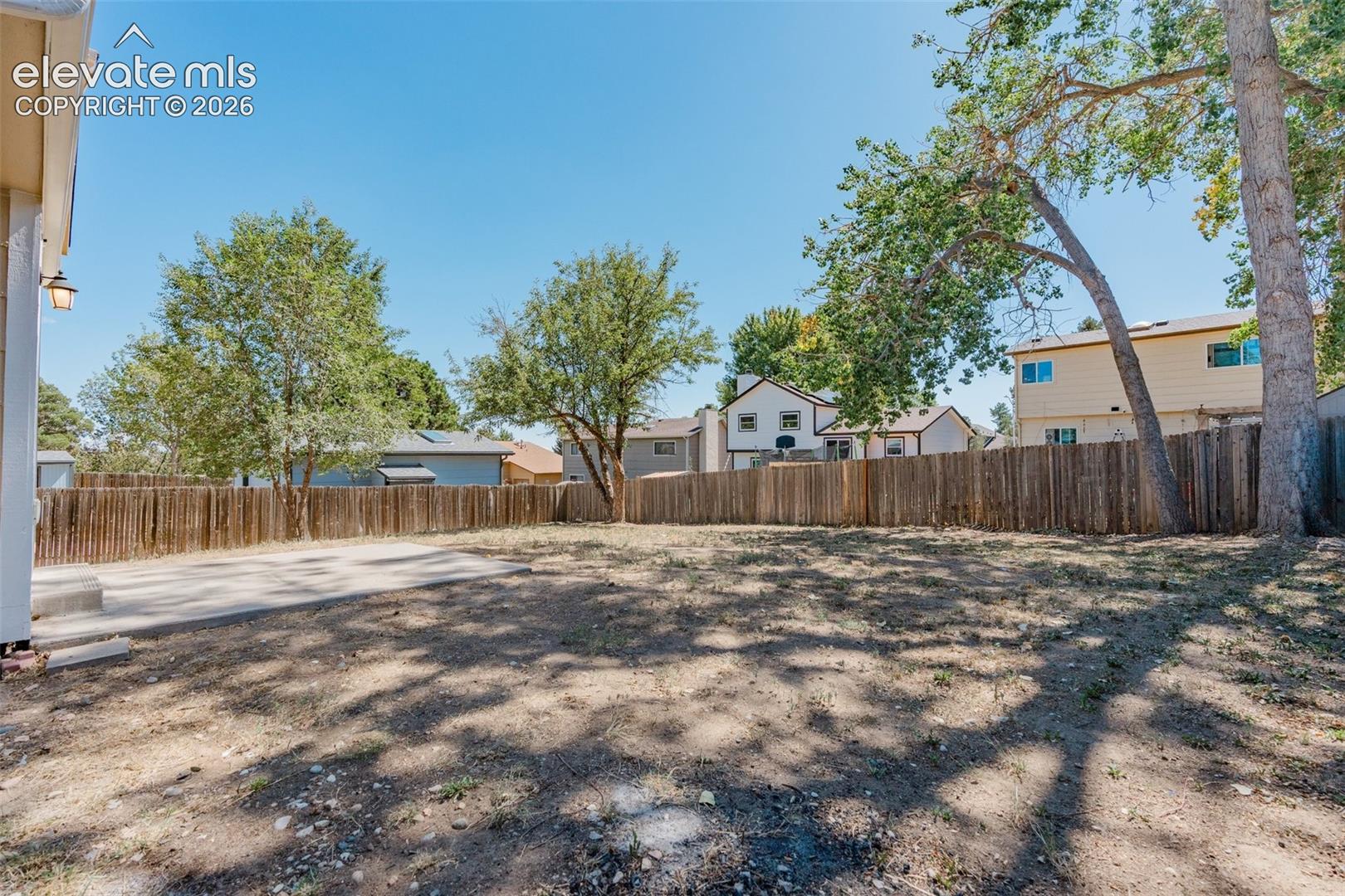 Expansive backyard featuring a wood fence, mature trees, and a concrete patio