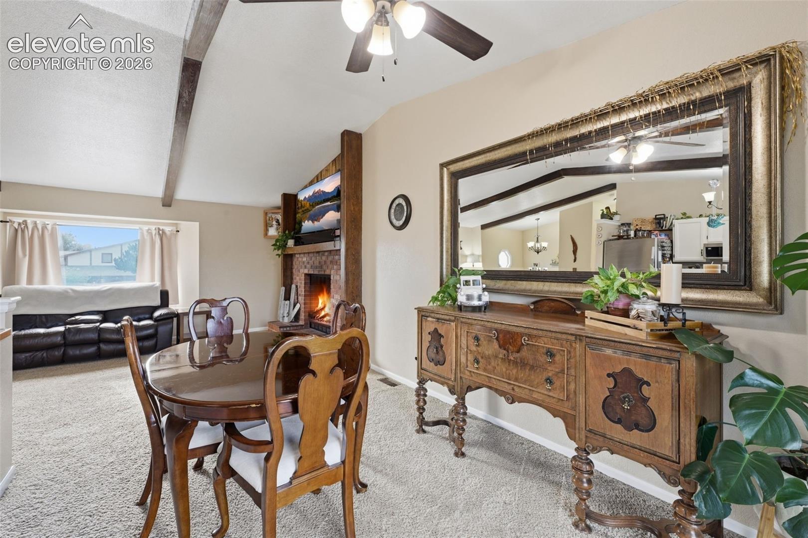 Vaulted ceilings with exposed wood beams, a fireplace with a stone-tile surround, and a ceiling fan with integrated lighting