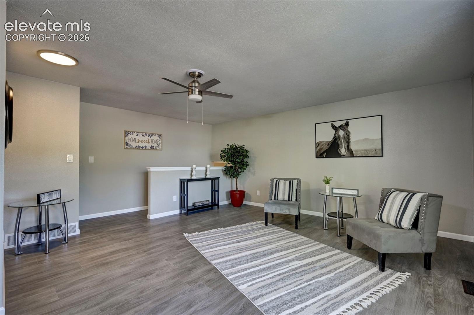 Neutral-toned living space featuring wood-finish flooring, a contemporary ceiling fan, and a low-profile pony wall with a built-in ledge
