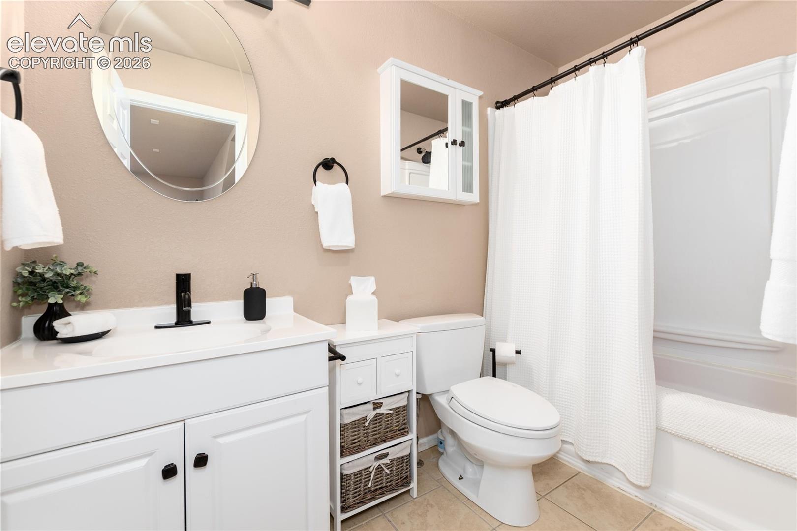 Bathroom featuring a white vanity with integrated sink, black single-handle faucet, oval wall-mounted mirror, white medicine cabinet, and a shower-tub combination with white enclosure