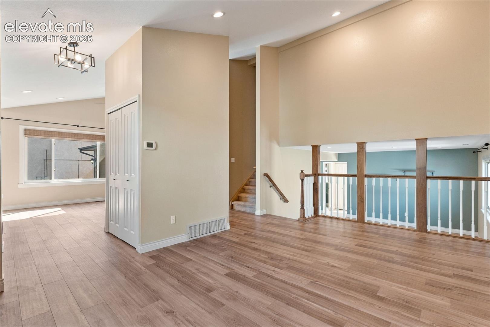 Vaulted ceilings featuring wood-finish flooring, recessed lighting, a modern geometric chandelier, and a wood-railing staircase with white balusters