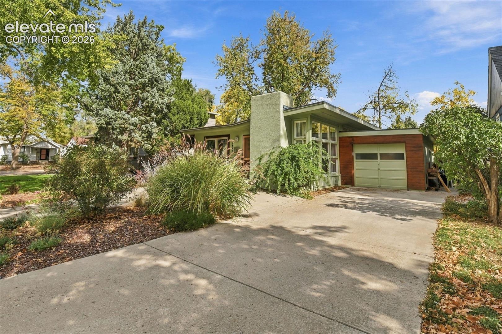Mid-century modern architectural style featuring an integrated garage, brick masonry accents, a prominent exterior chimney, and large multi-pane windows