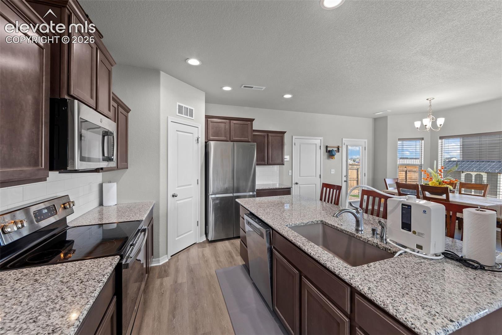 Kitchen featuring dark wood-finish cabinetry, stainless steel appliances, granite countertops, and wood-finish flooring
