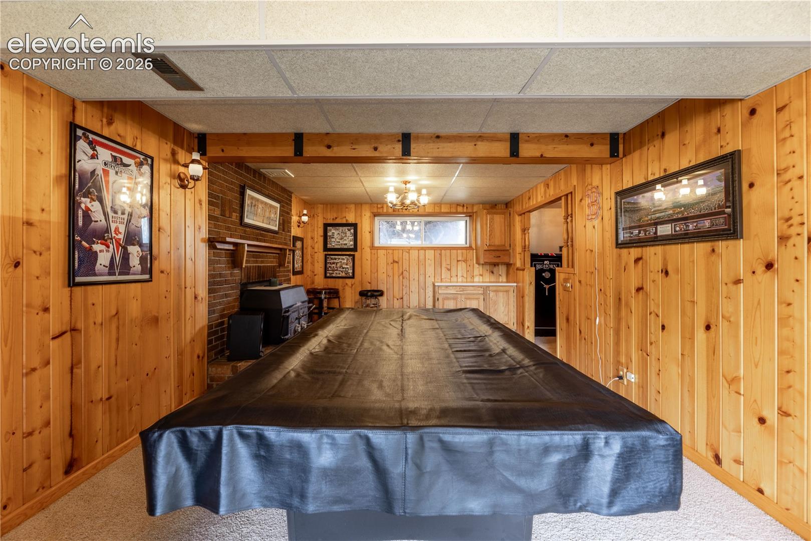 Interior space featuring knotty pine wall paneling, a brick fireplace surround, exposed wood beam detailing, and recessed multi-light fixture