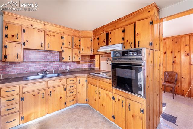 Kitchen with oven, under cabinet range hood, decorative backsplash, white electric stovetop, and wooden walls