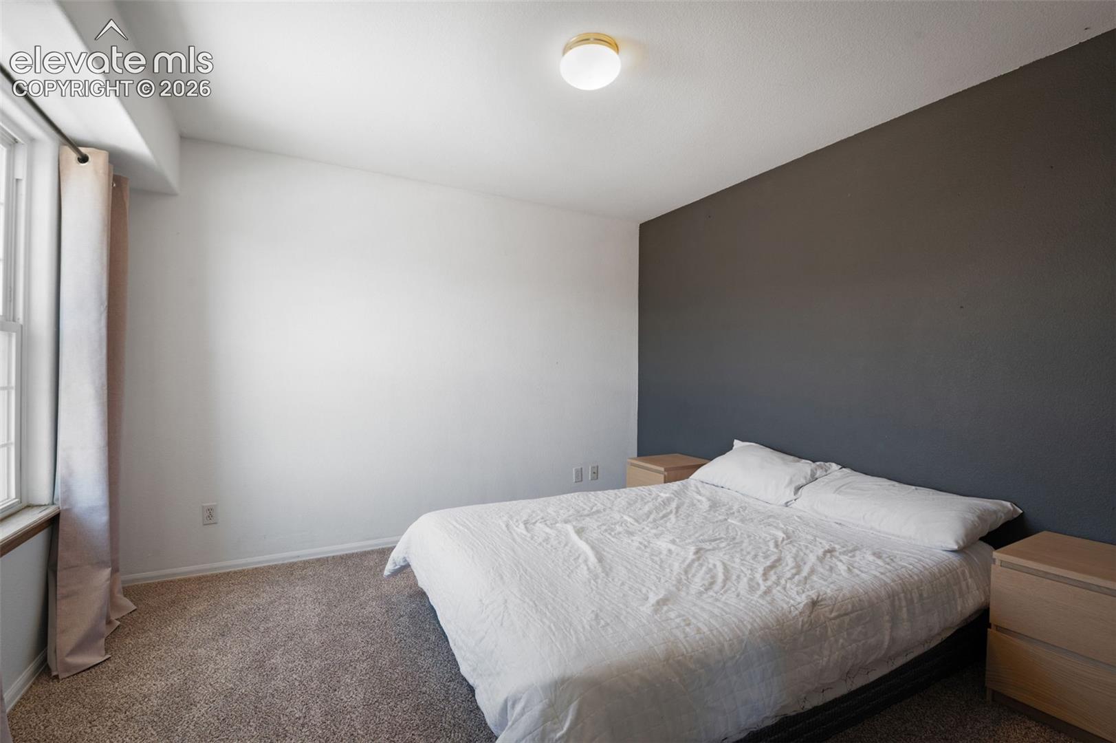 Bedroom featuring a statement accent wall, carpeted flooring, and a window with a sill