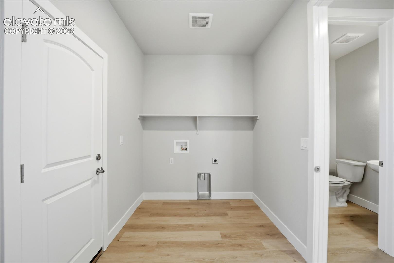 Utility room featuring wood-finish flooring, a wall-mounted storage shelf, and dedicated water and electrical hookups