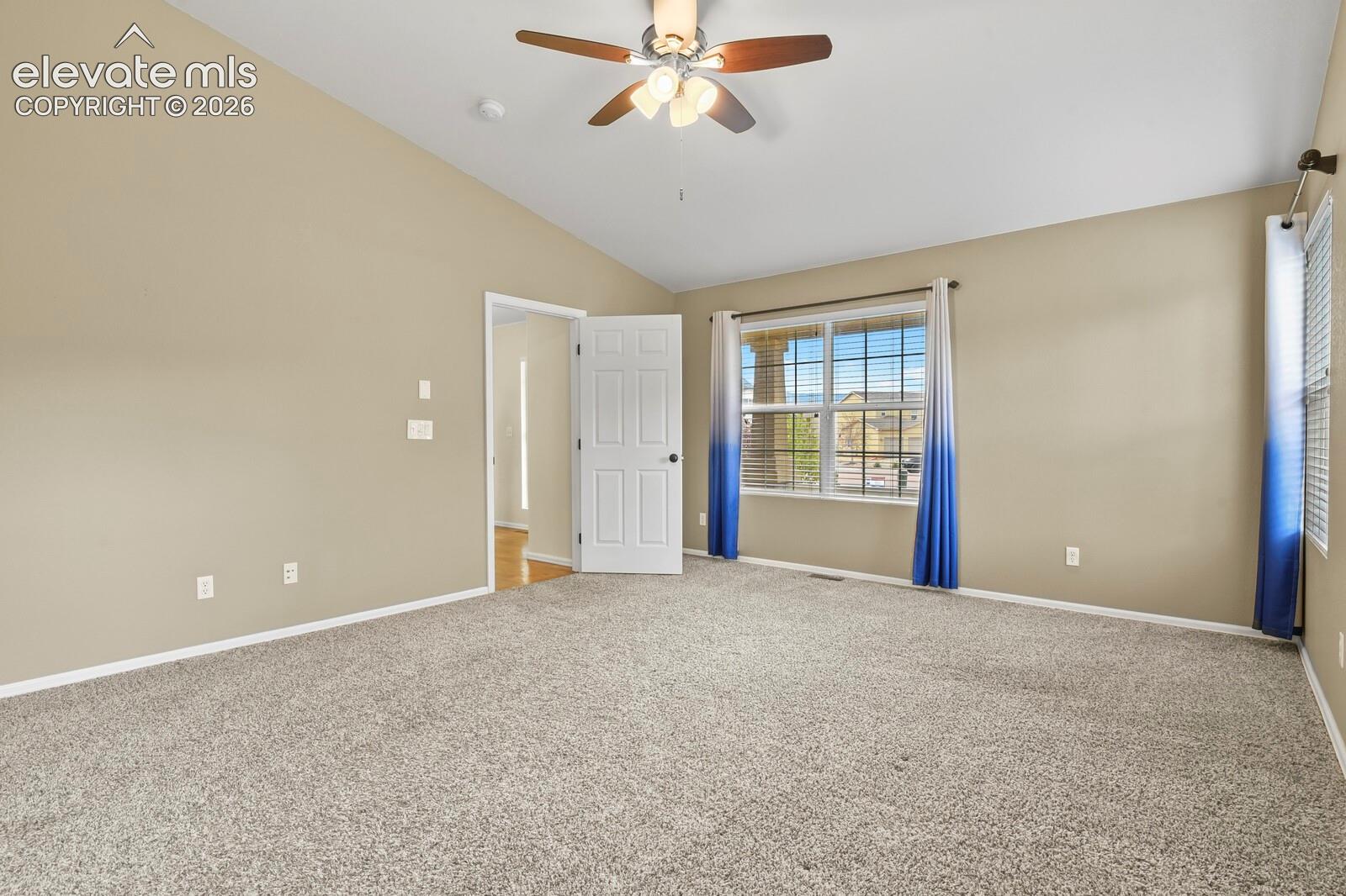 Spacious room featuring vaulted ceilings, neutral wall tones, and plush carpet flooring