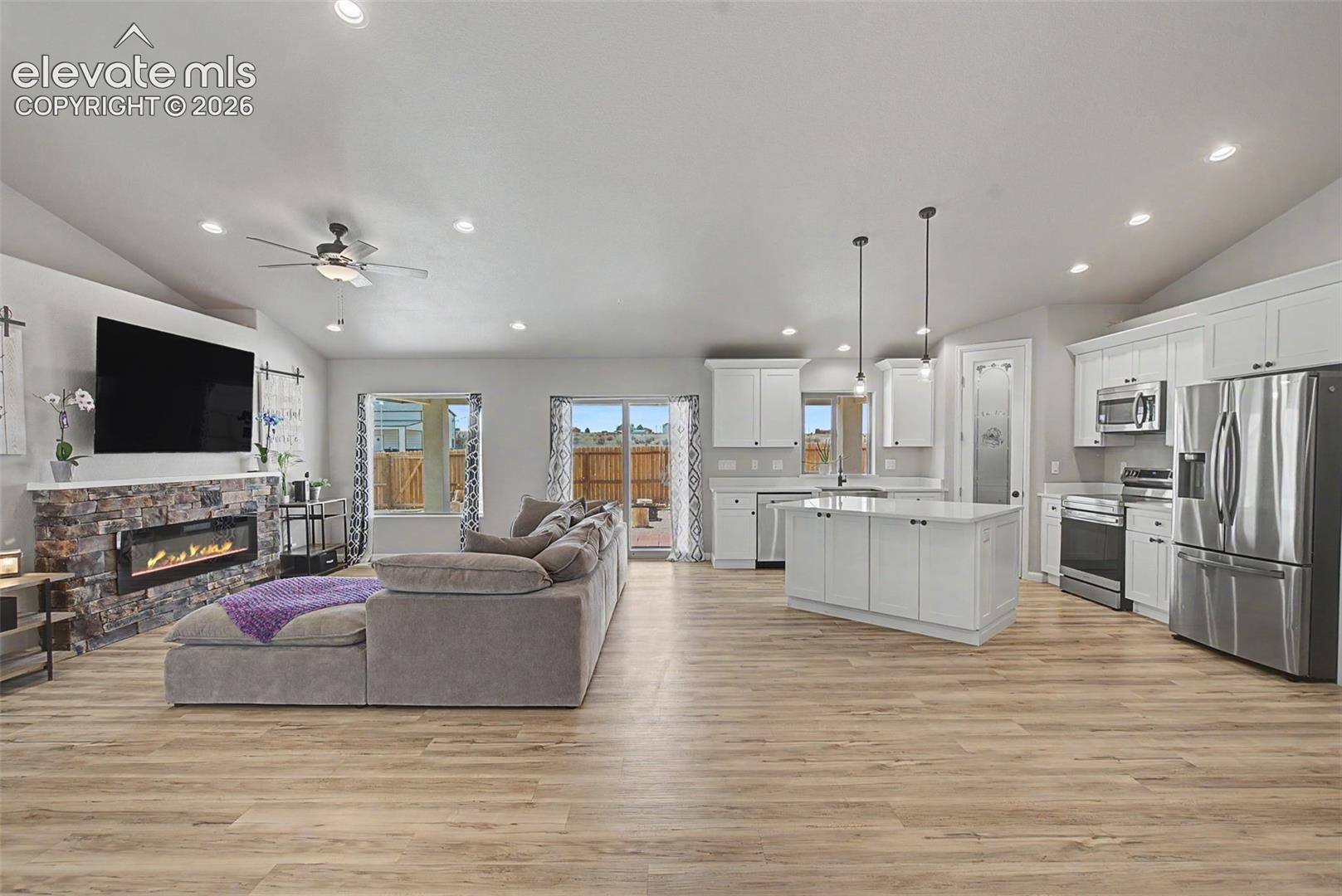 Open-concept living space featuring wood-finish flooring, a stone-faced fireplace, a vaulted ceiling, and recessed lighting