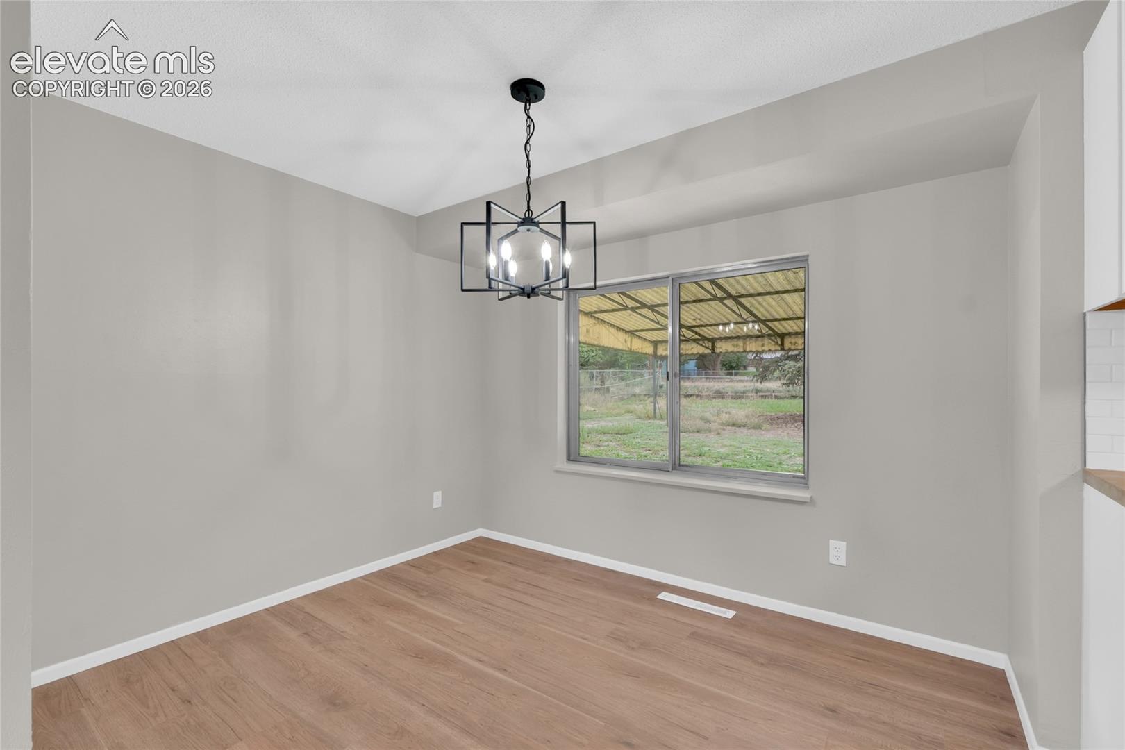 Wood-finish flooring, contemporary black chandelier, neutral wall tones, and a sliding window