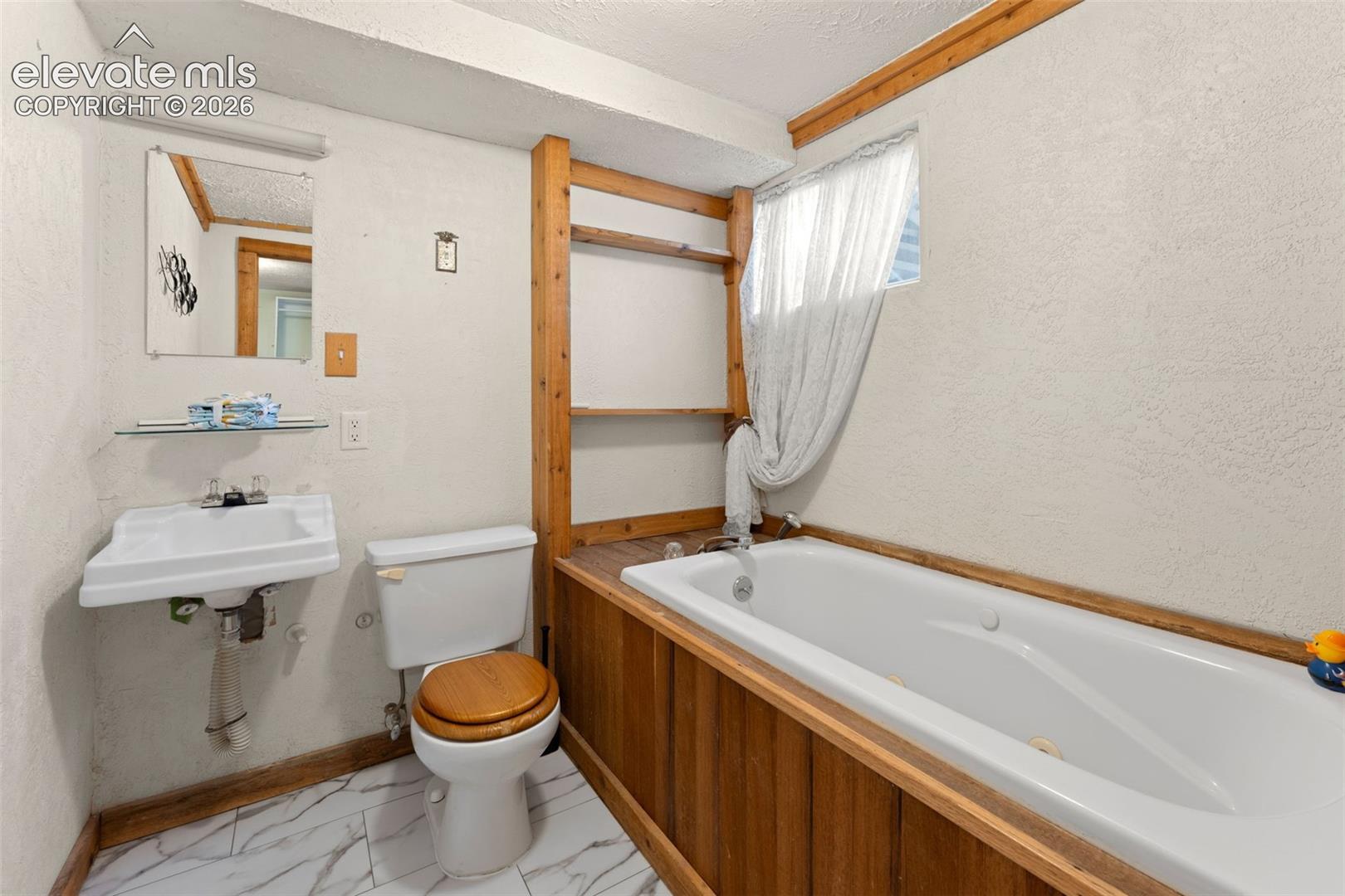 Pedestal sink, wall-mounted mirror, built-in shelving, white bathtub, and wood-finish paneling