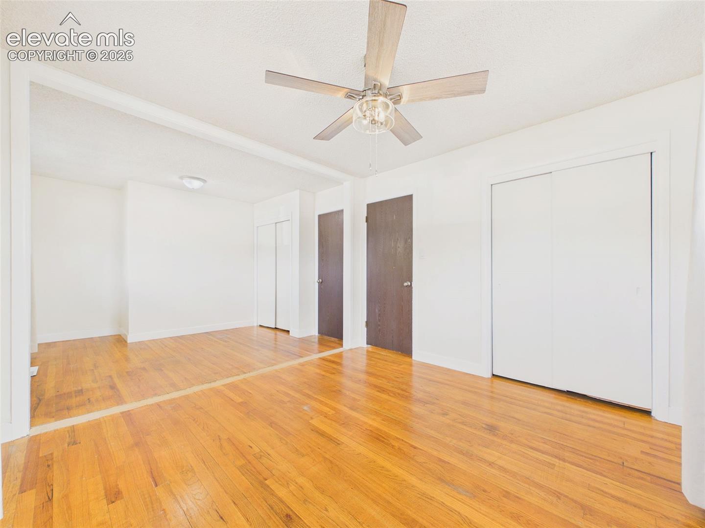 Additional view of the oversized bedroom, originally configured as two separate rooms, featuring hardwood flooring, a ceiling fan, and multiple closets.