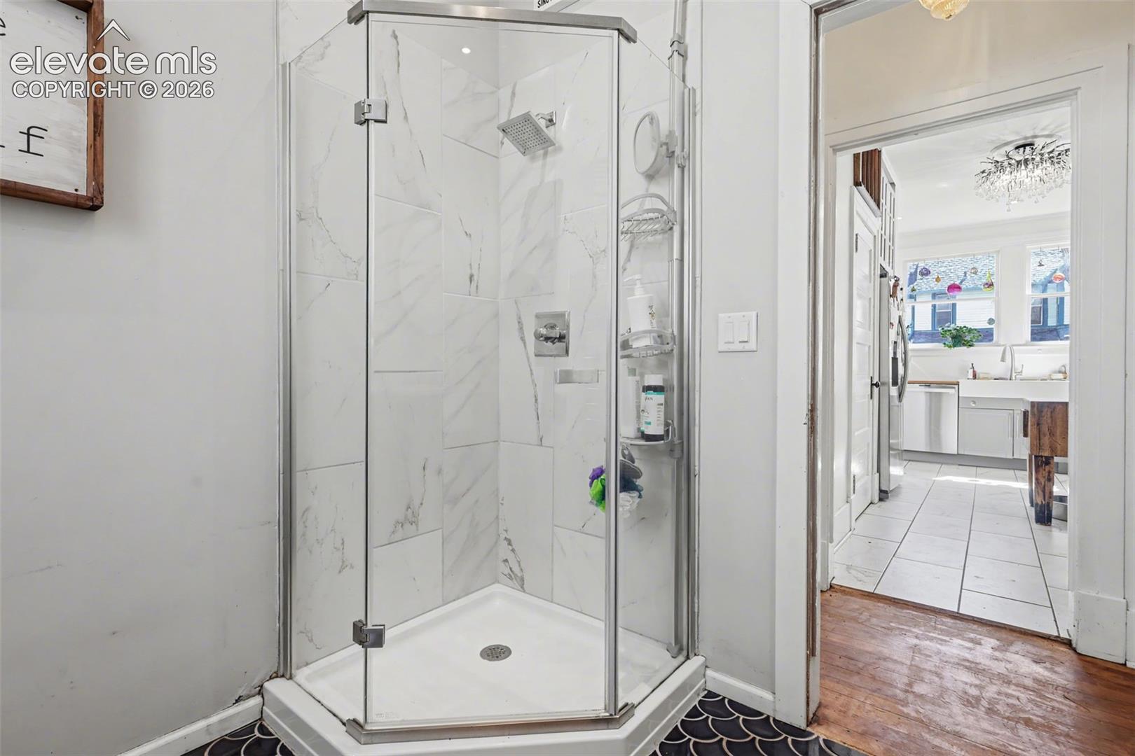 Bathroom with a marble finish shower, hanging lights, and dark tile patterned flooring