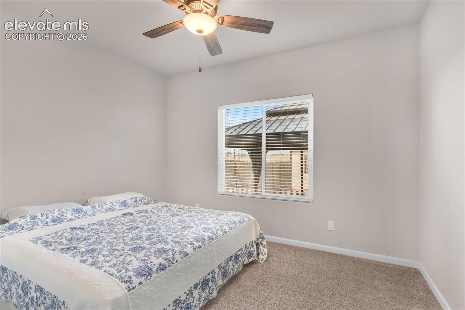 Bedroom featuring neutral wall tones, plush carpeting, a multi-pane window with horizontal blinds, and a ceiling fan with integrated lighting