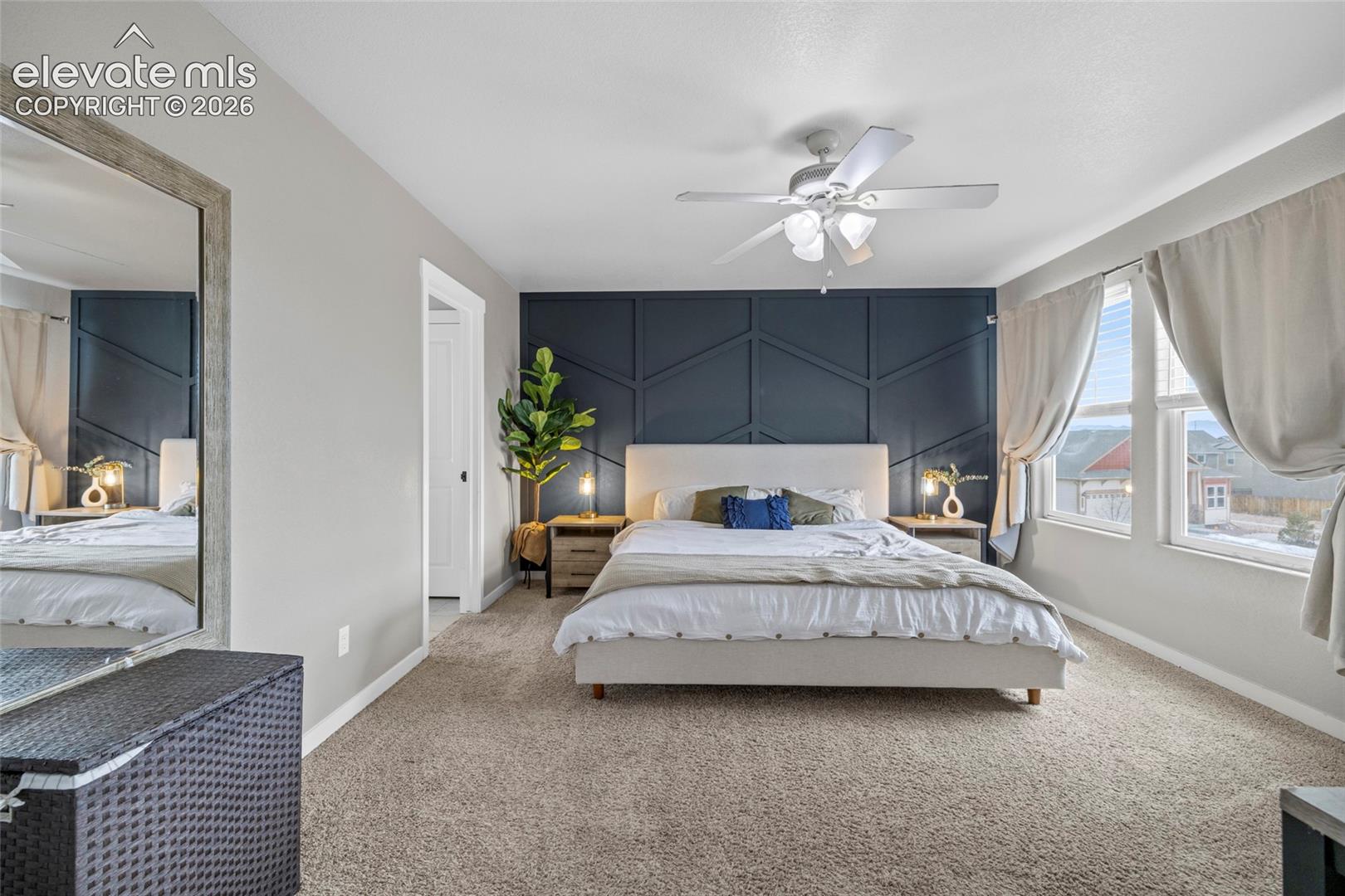 Bedroom featuring a dark accent wall with geometric millwork, neutral carpeting, and a multi-blade ceiling fan with integrated lighting