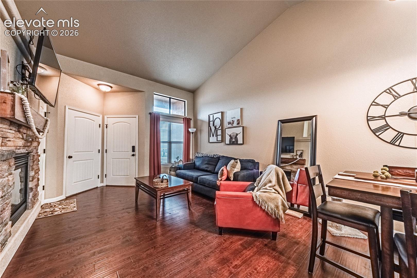Living area featuring dark wood finished floors, a stone fireplace, and high vaulted ceiling