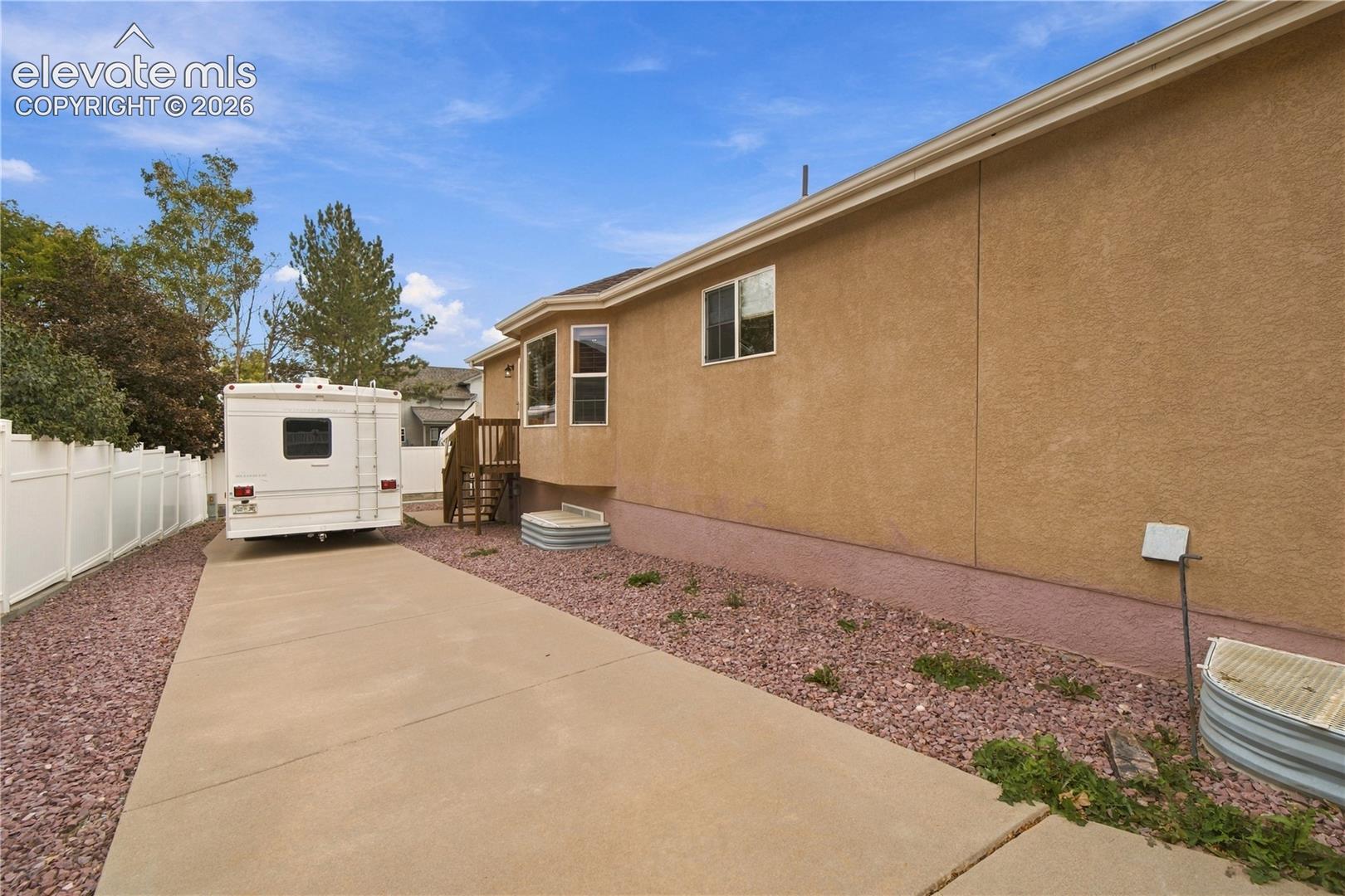 Stucco exterior featuring a concrete driveway, ground-level window wells, and white vinyl privacy fencing