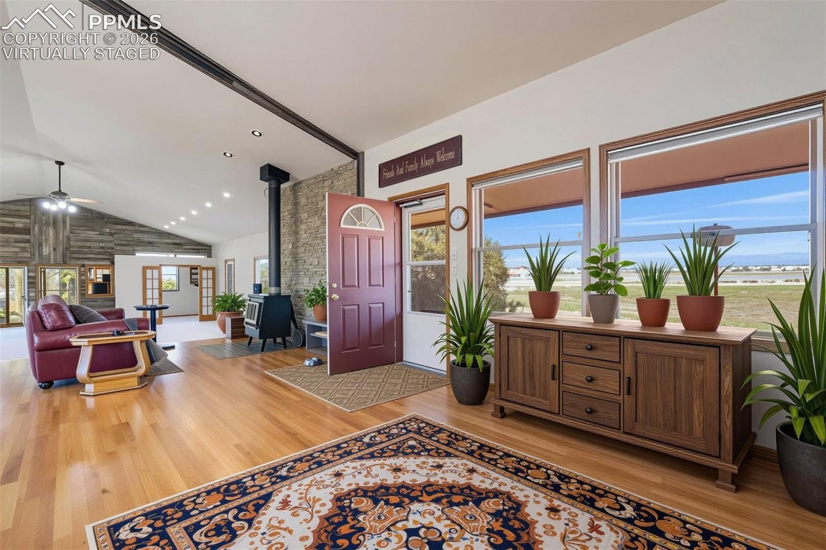 virtually staged Open concept interior featuring hardwood flooring, a vaulted ceiling, and a stone accent wall with a wood-burning stove