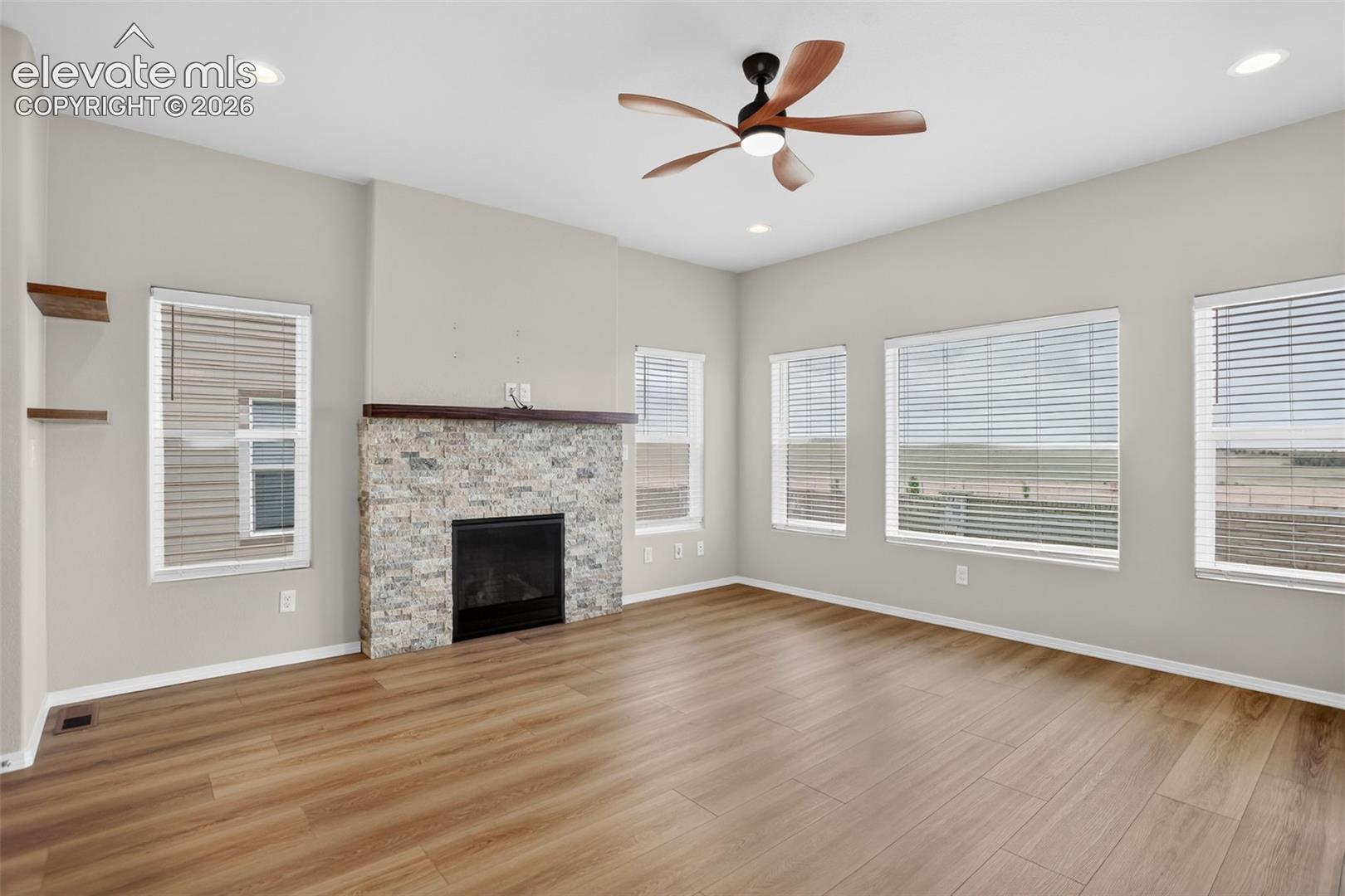 Spacious living area featuring wood-finish flooring, a stone-faced fireplace with a wood mantle, and multiple large windows