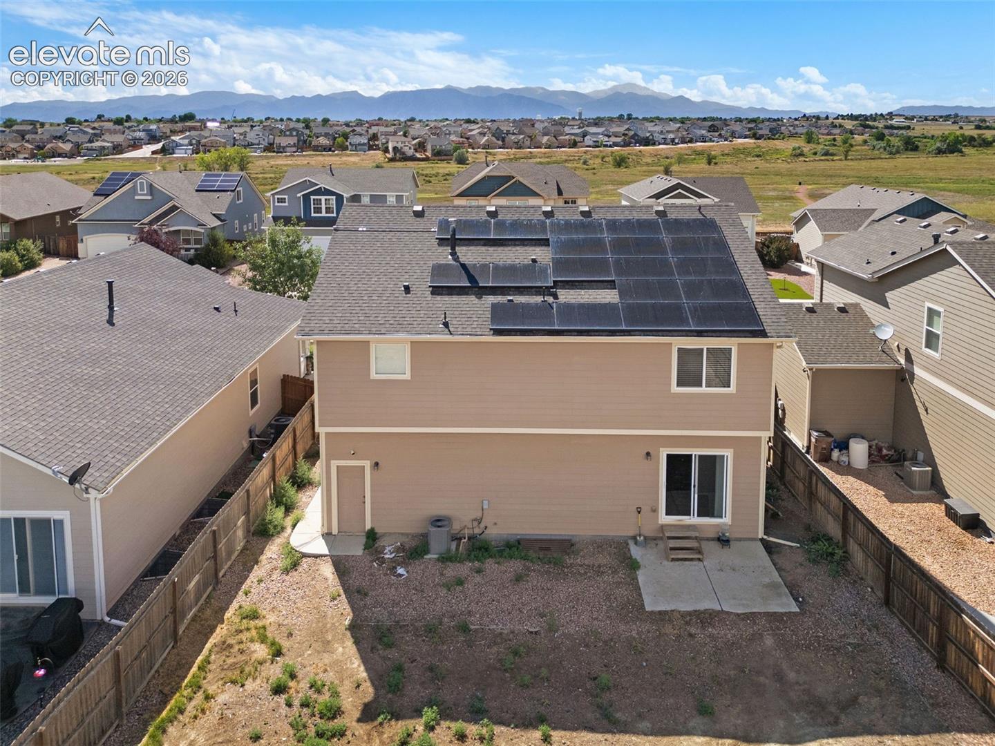 Rear exterior featuring installed solar panels, composite shingle roof, horizontal siding, concrete patio, and fenced perimeter