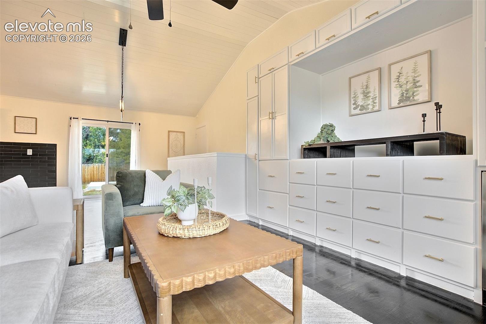 Vaulted ceilings, expansive floor-to-ceiling built-in storage cabinetry, dark-finish flooring, black brick fireplace surround, and sliding glass door