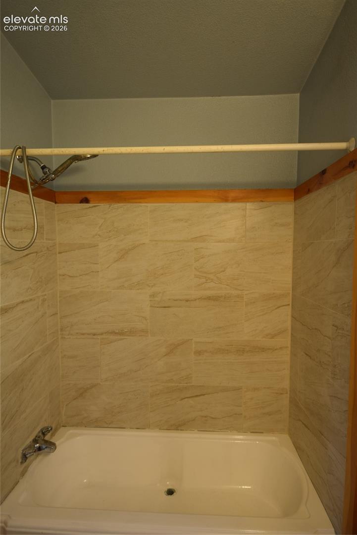Tub/shower combination featuring a chrome shower head with a flexible hose and subway-style tile surround