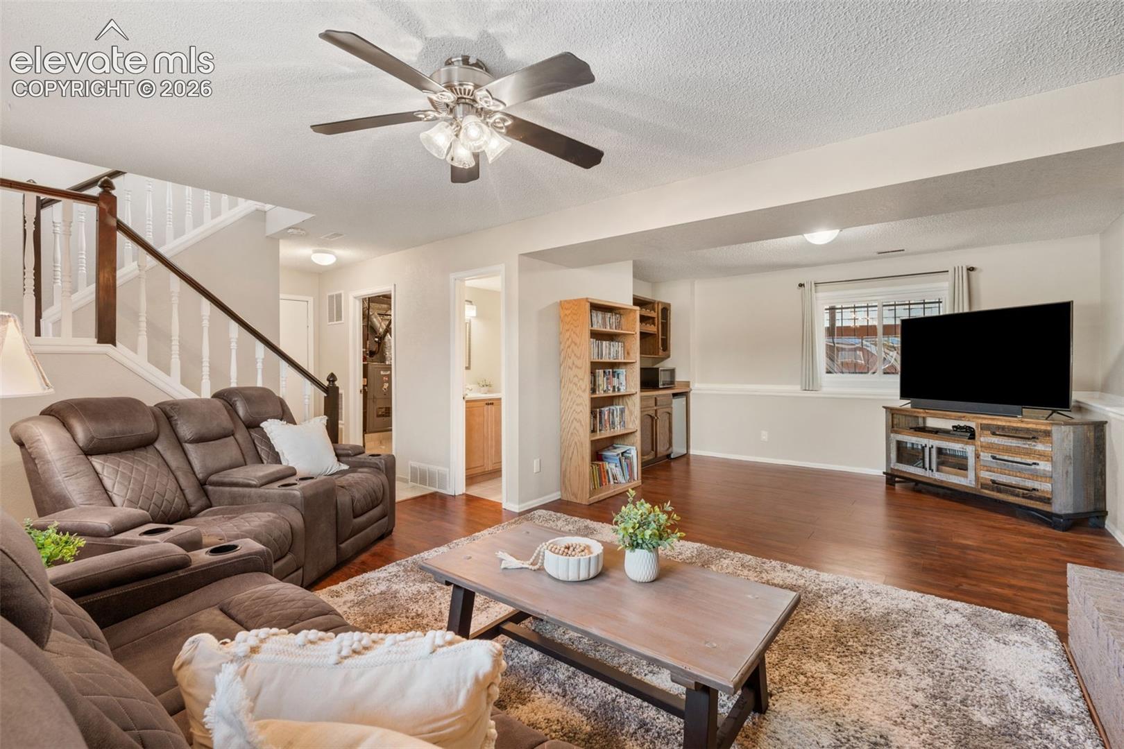Wood-finish flooring, ceiling fan with integrated lighting, staircase with decorative balusters, built-in cabinetry, and neutral wall tones