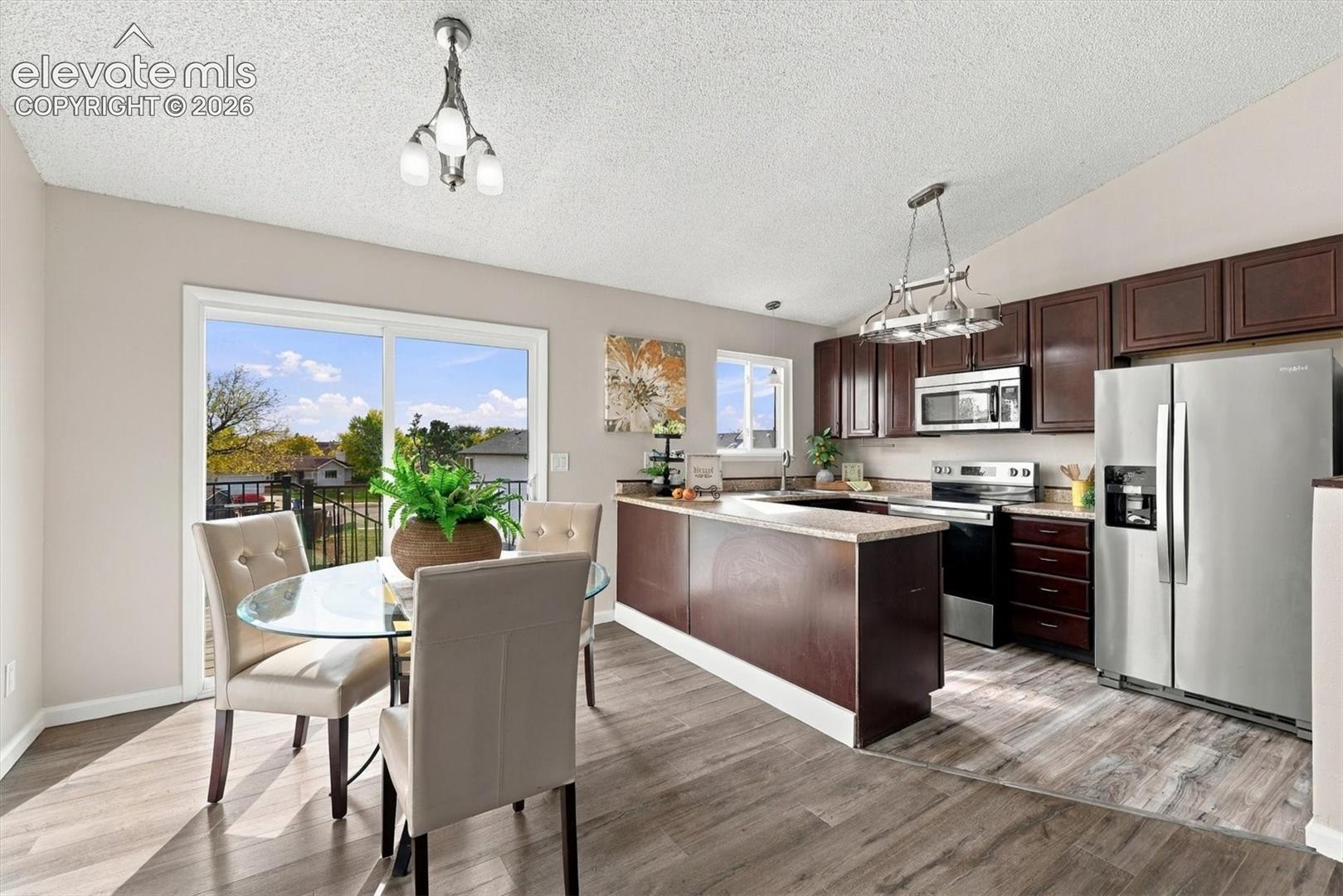 Kitchen featuring dark wood cabinetry, stainless steel appliances, wood-finish flooring, a breakfast bar, and glass sliding doors