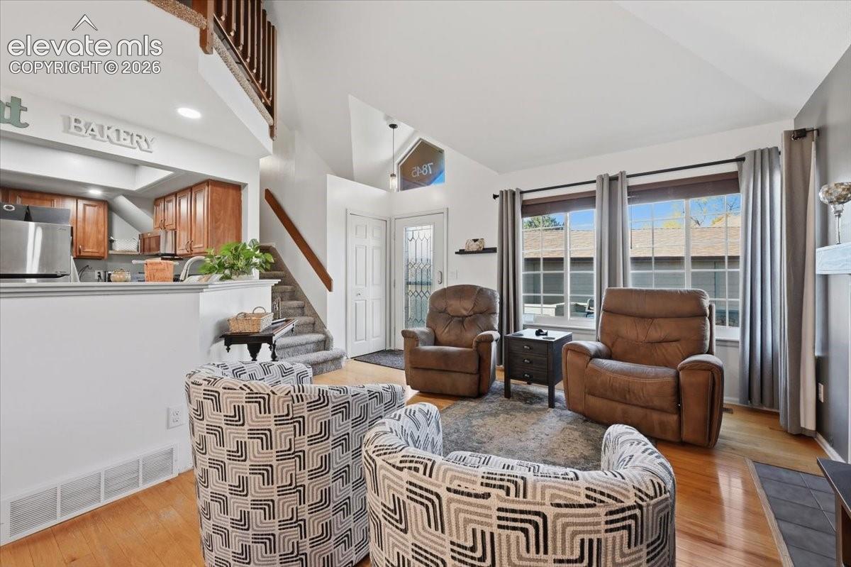 Vaulted ceilings, expansive windows with grid detailing, wood-finish flooring, staircase with a wooden handrail, and built-in kitchen cabinetry