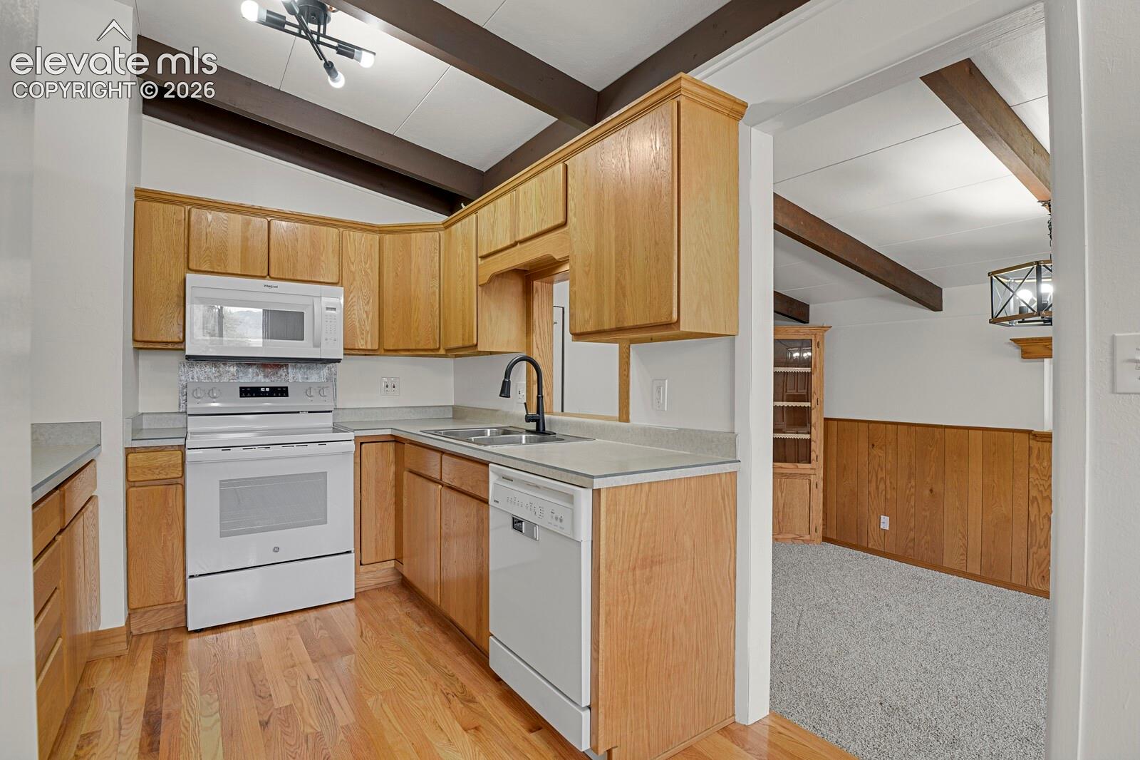 Kitchen featuring wood cabinetry, solid-surface countertops, wood-finish flooring, exposed ceiling beams, and a matte black faucet