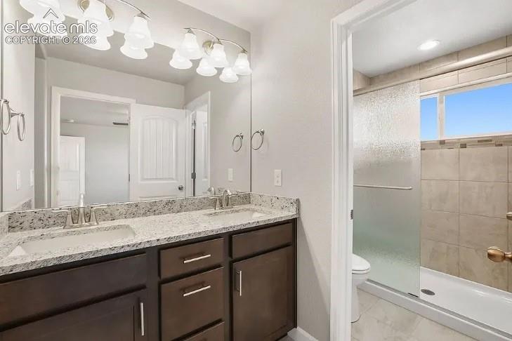 Double vanity featuring stone countertops, integrated dual sinks, dark cabinetry with metallic hardware, and a walk-in shower with tiled surround and glass enclosure