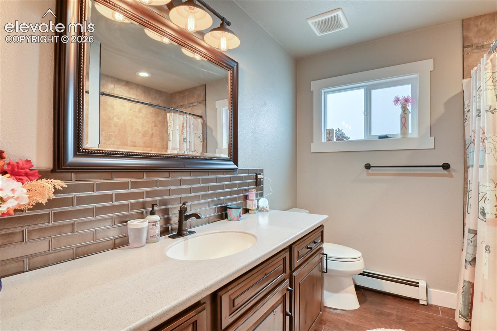 Bathroom with backsplash, vanity, a baseboard radiator, light wood-style flooring, and a shower with curtain