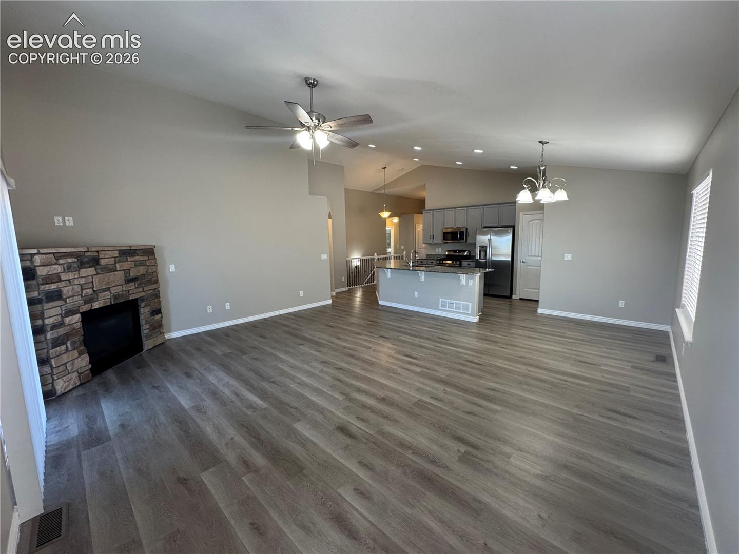 Vaulted ceilings, wood-finish flooring, stone-veneer fireplace, recessed lighting, and kitchen island with granite-surfaced breakfast bar