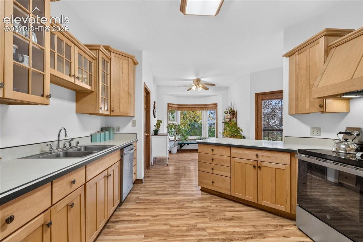 Kitchen featuring natural wood cabinetry, solid surface countertops, wood-finish flooring, glass-front upper cabinet doors, and a bay window