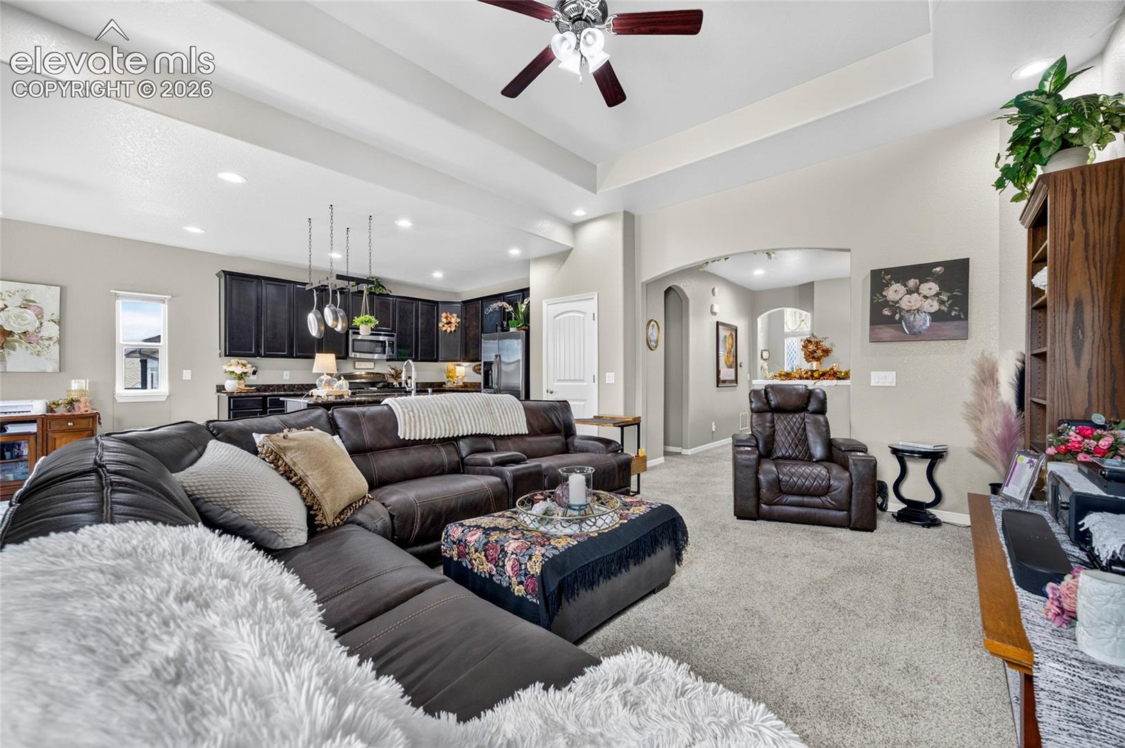 Tray ceiling, recessed lighting, ceiling fan, arched doorway, and dark-toned cabinetry