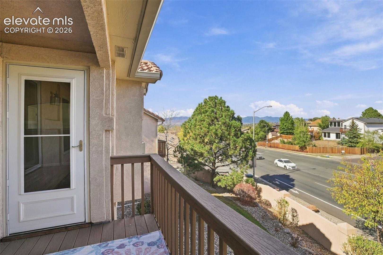 Covered balcony featuring wood-finish decking, wooden railing, and a full-light glass storm door