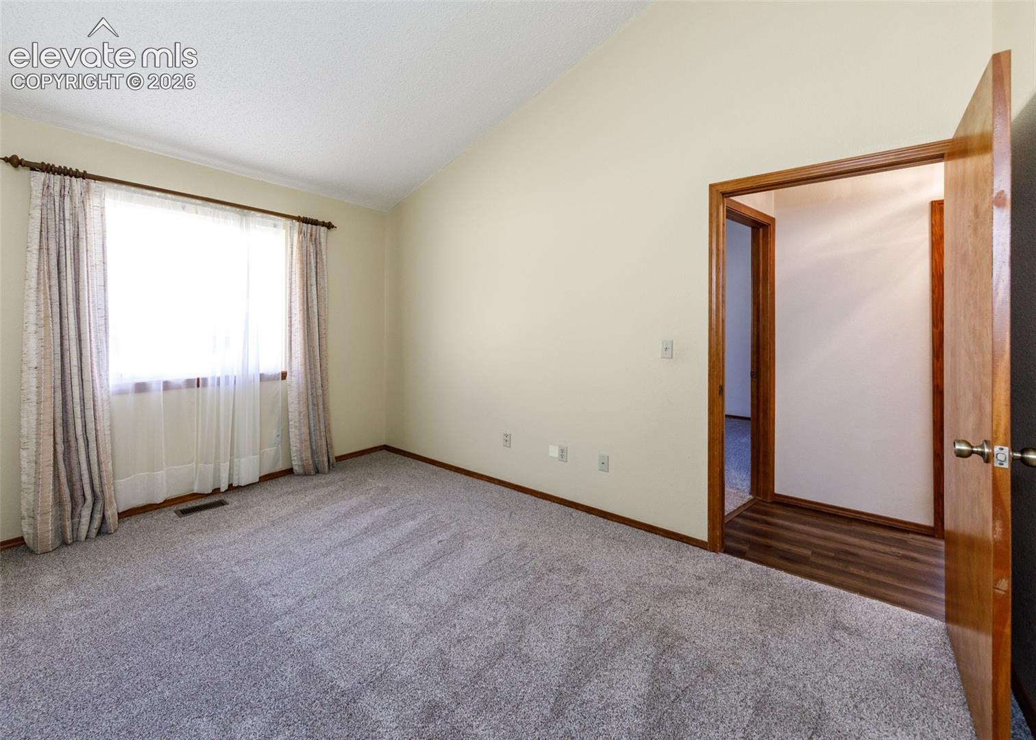 Vaulted ceiling, wall-to-wall carpeting, wood-trim window with drapes, and wood-trim doorways