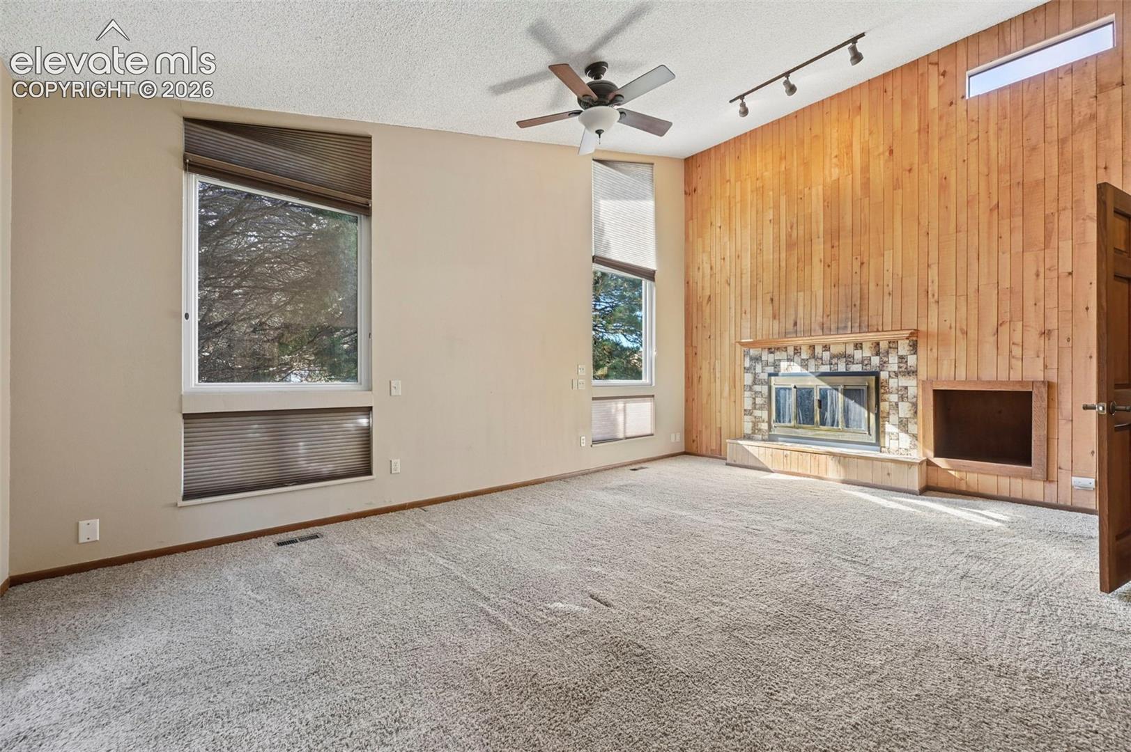Vaulted ceilings, floor-to-ceiling wood-panel accent wall, fireplace with stone surround, built-in shelving, and multi-level windows