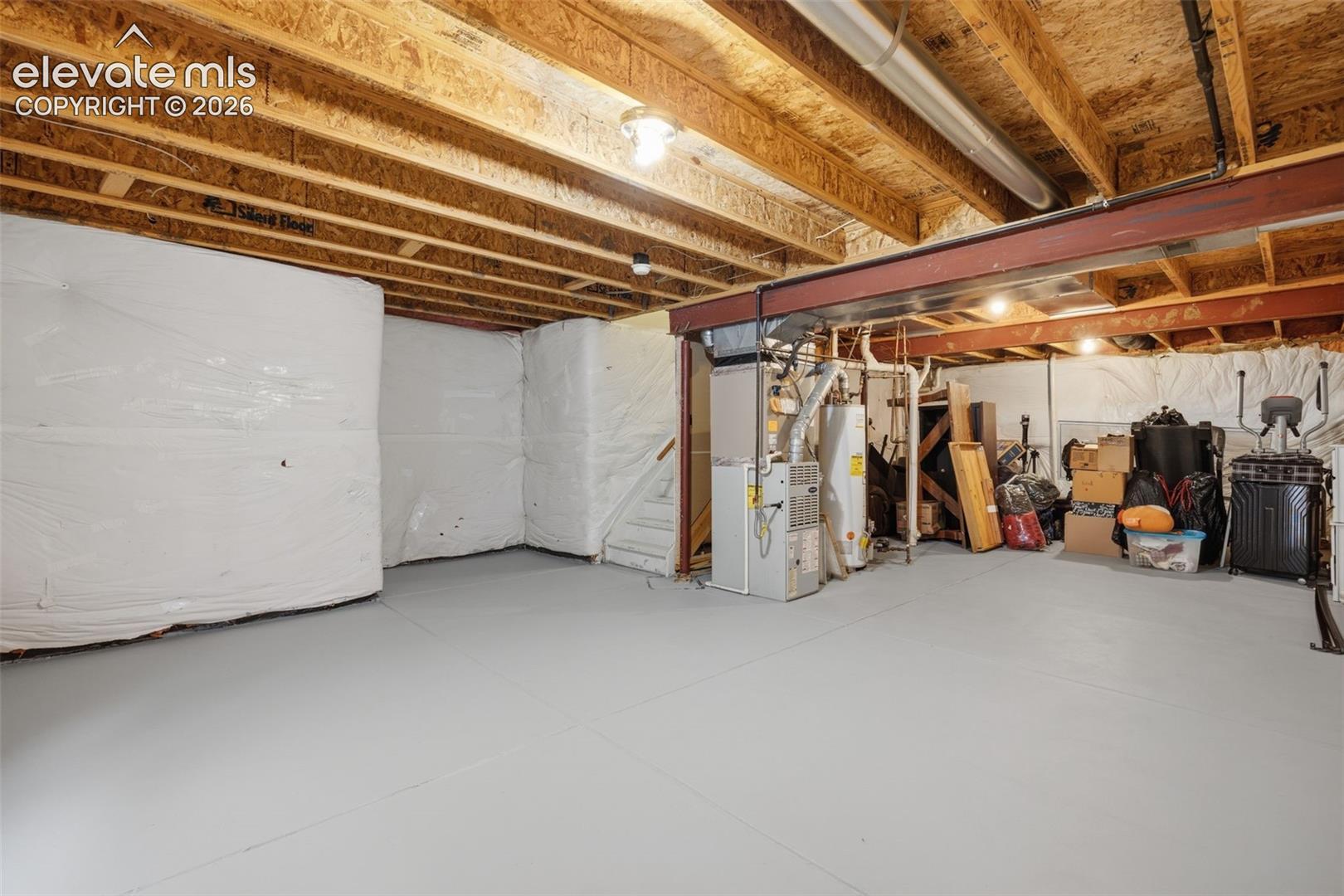 Unfinished basement with exposed wood joists, painted concrete flooring, and visible utility systems