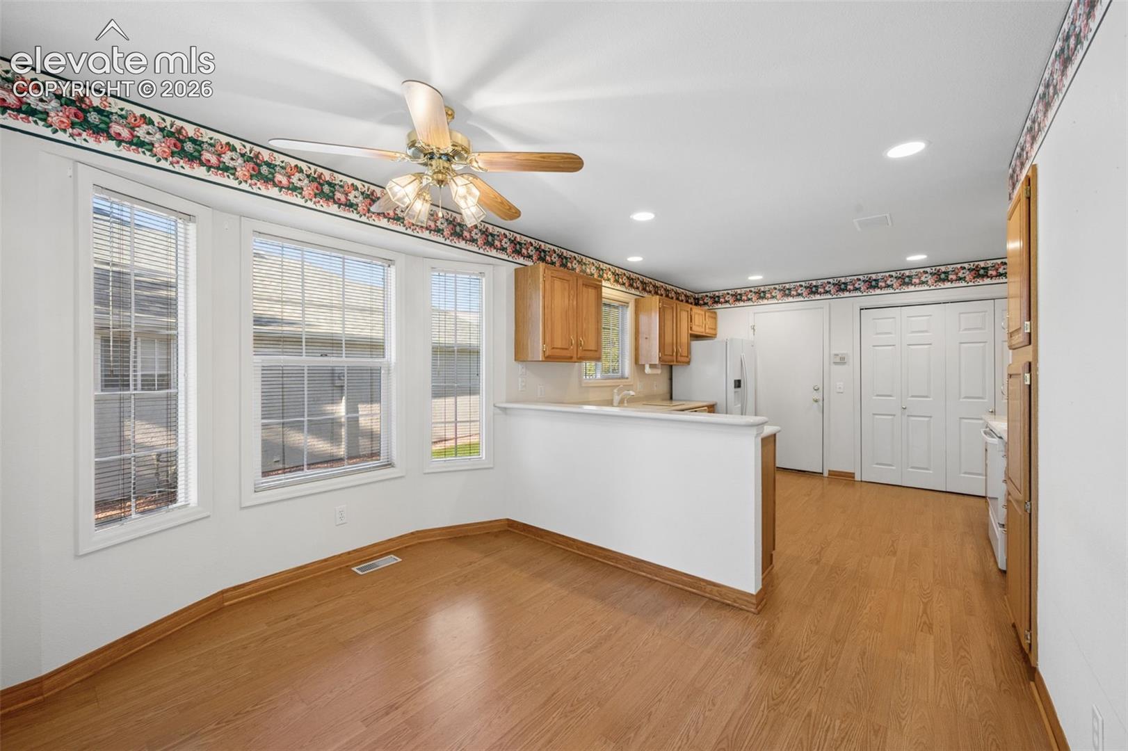 Kitchen featuring wood-finish flooring, a bay window, ceiling fan with light fixture, breakfast bar, and wood cabinetry