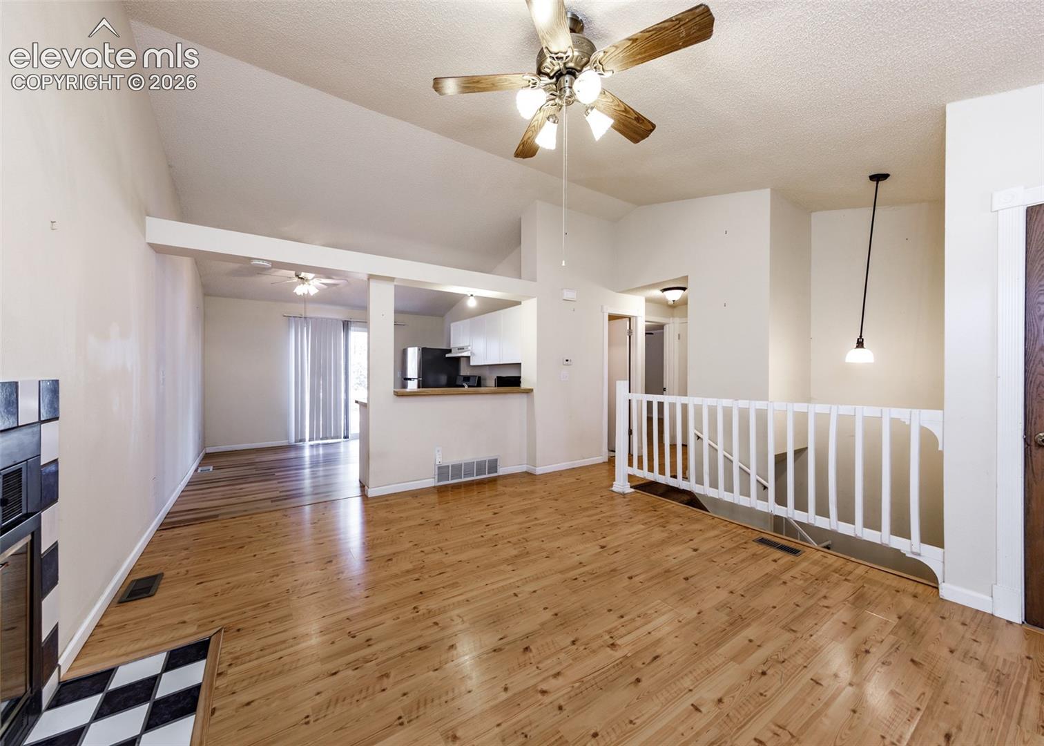 Vaulted ceiling featuring a central wood-finish ceiling fan, wood-finish flooring, fireplace with a tiled surround, and a wooden stair railing
