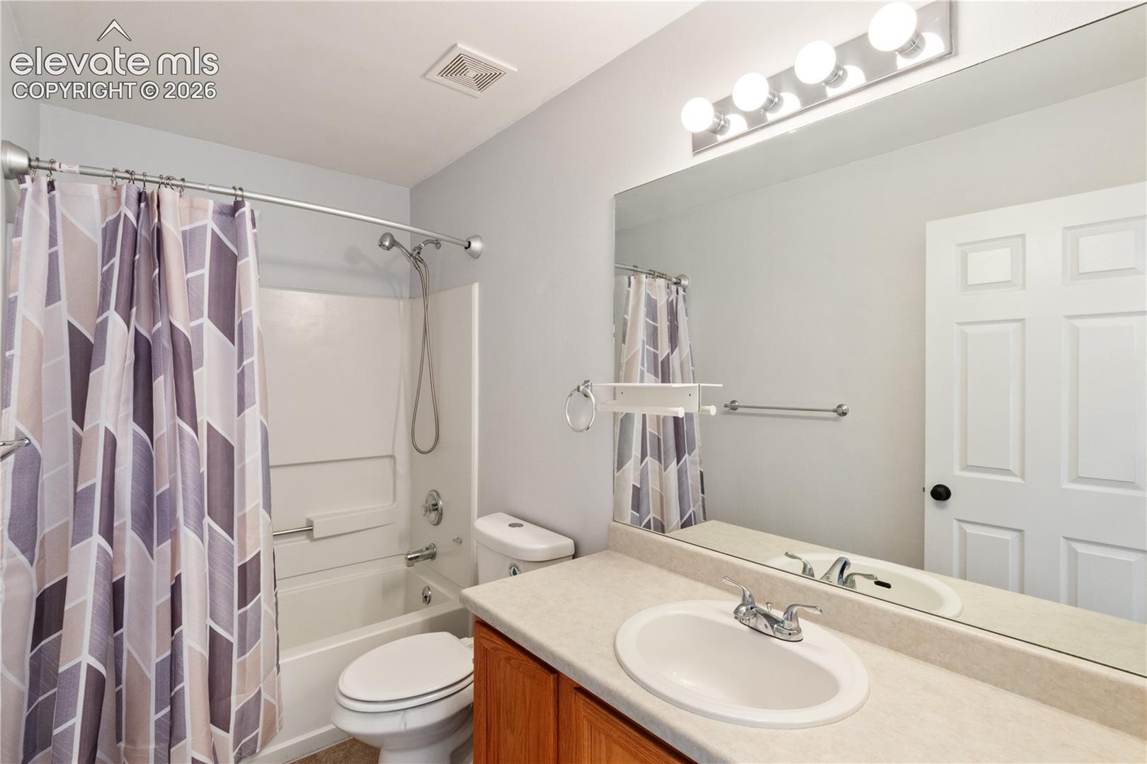 Bathroom featuring a single-sink vanity with a solid-surface countertop, an expansive wall-to-wall mirror, an integrated tub and shower combination, and a five-light vanity fixture