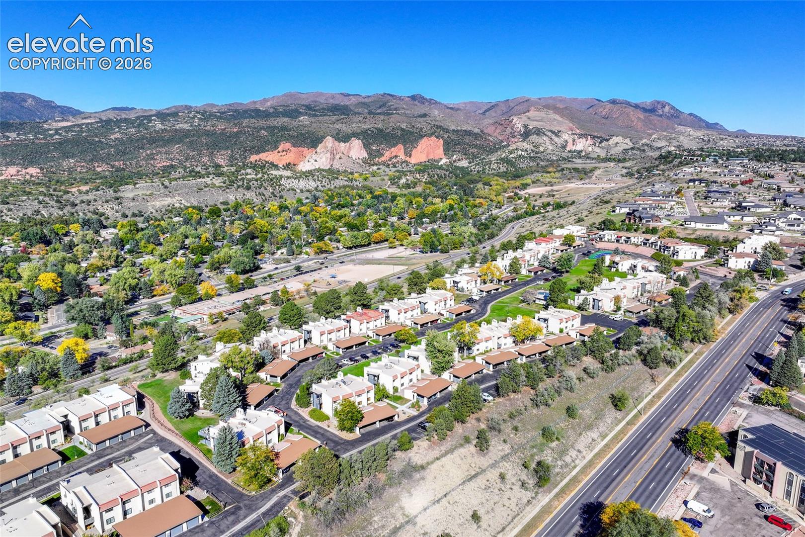 Aerial perspective of the property featuring multi-family residential structures, integrated carport parking, paved site circulation, and landscaping, set against a prominent mountain and rock formation backdrop