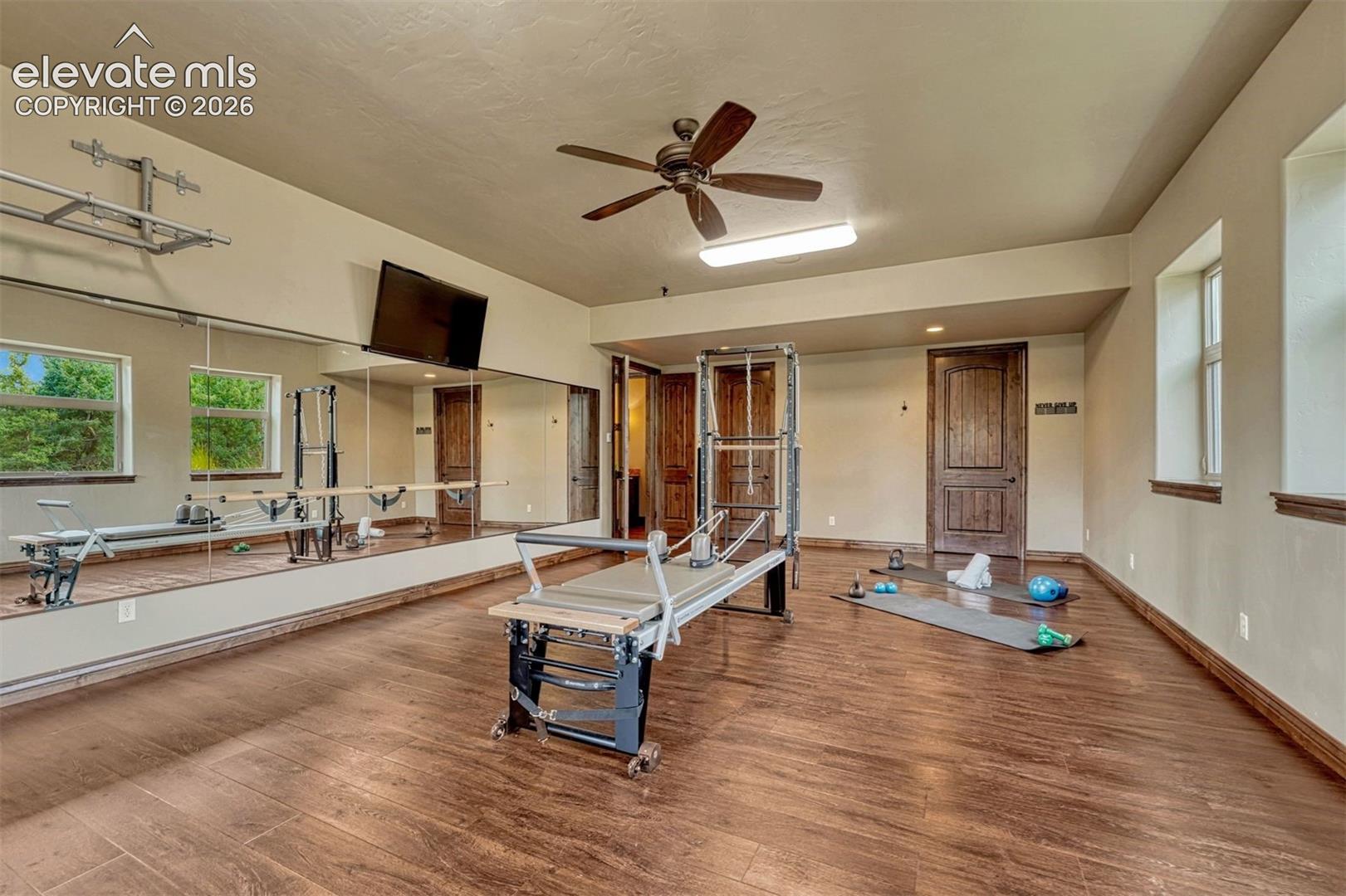 Dedicated exercise space featuring wood-finish flooring, full-wall mirrors, recessed lighting, and a ceiling fan