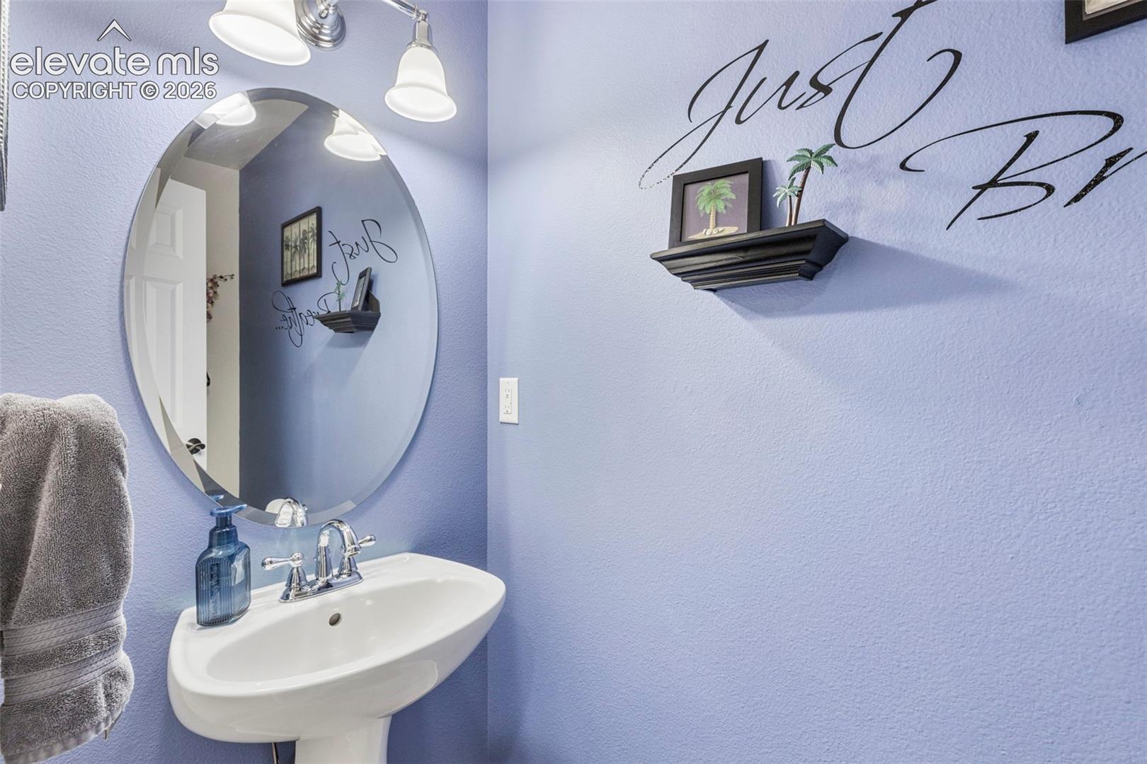 Pedestal sink with chrome faucet, oval mirror, and wall-mounted light fixture