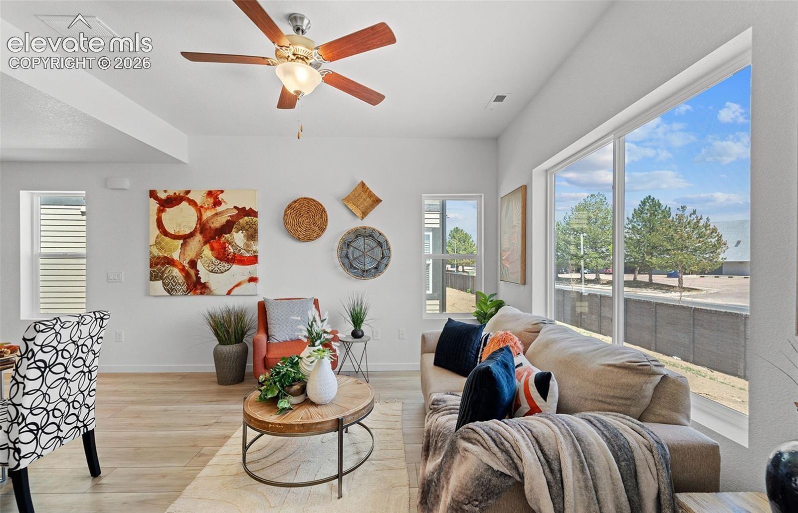 Open-concept living space featuring wood-finish flooring, a ceiling fan with integrated lighting, and a large picture window