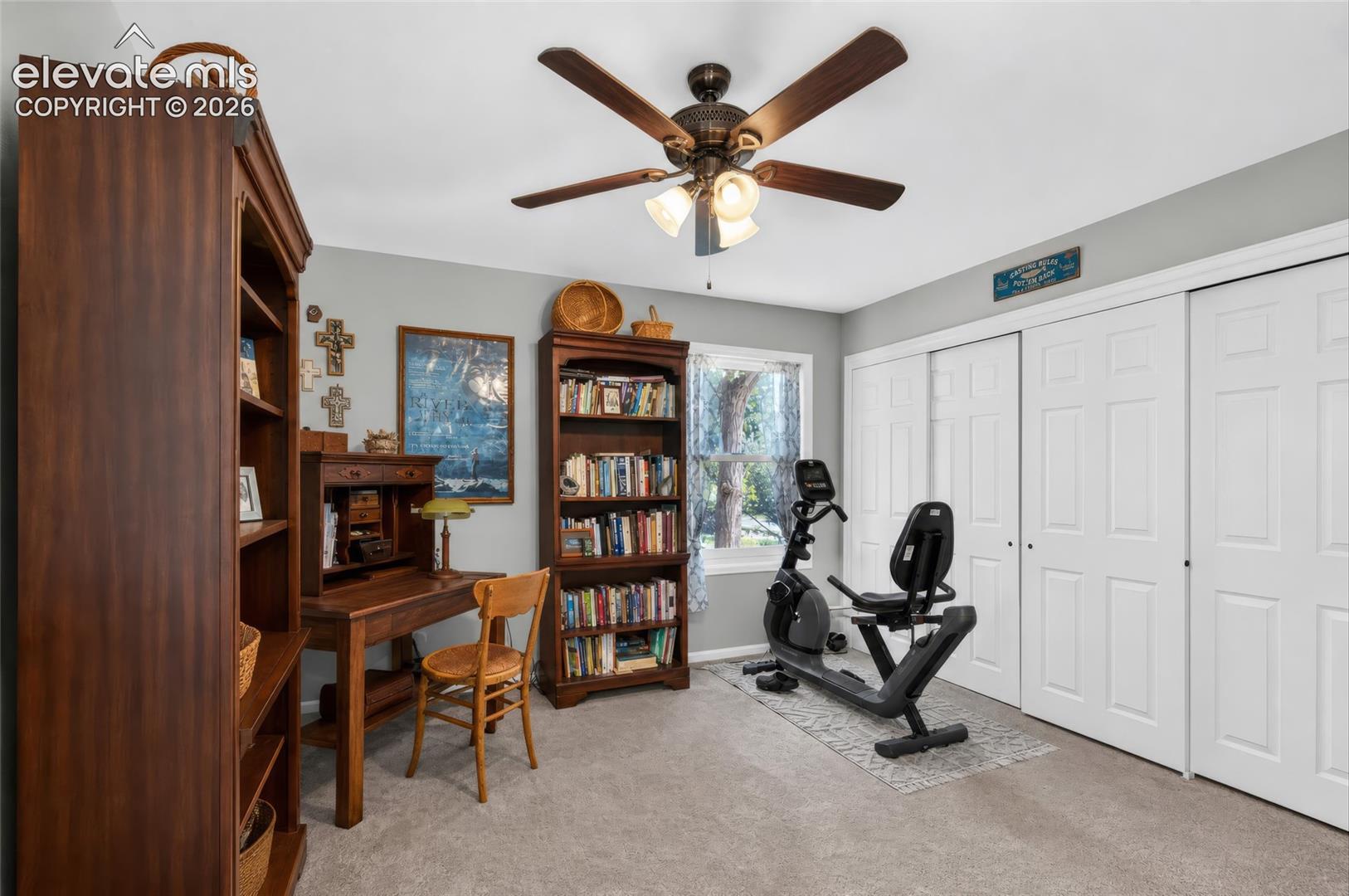 Carpeted flooring, a window offering natural light, two sets of white bi-fold closet doors, and a ceiling fan with integrated lighting